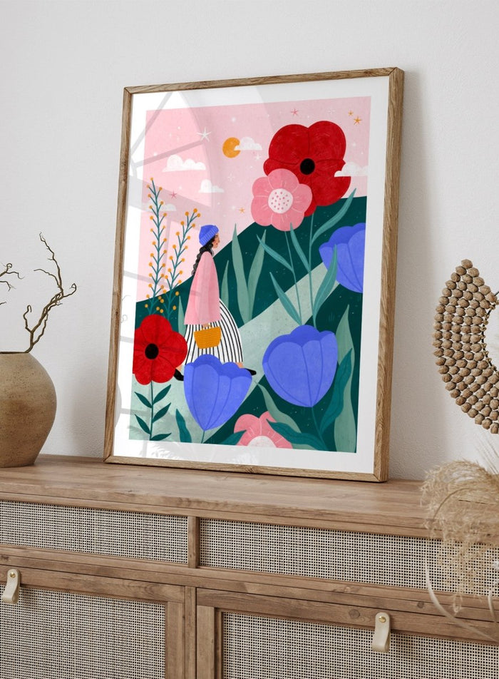 A framed art print featuring a whimsical, colorful illustration of a woman walking through a field of oversized flowers under a pink sky with moon. Whimsical Flower Path by Bea Müller premium fine art print featuring a woman walking among oversized flowers in a bright, playful landscape.