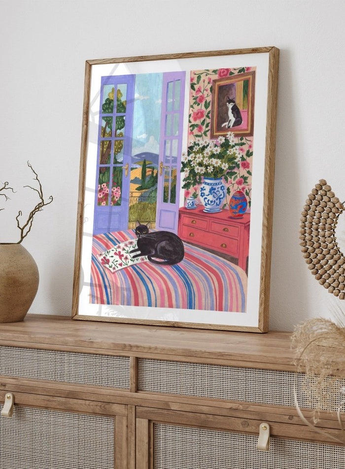 Cat lounging on a striped bed with a view of a garden through open doors, surrounded by flowers and decorative items. Black Cat on Bed French Doors Garden View by Caroline Bonne Müller is a colorful interior art print featuring cat illustration, floral room, and scenic garden view in a modern aesthetic style.