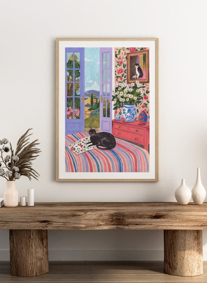 Cat lounging on a striped bed with a view of a garden through open doors, surrounded by flowers and decorative items. Black Cat on Bed French Doors Garden View by Caroline Bonne Müller is a colorful interior art print featuring cat illustration, floral room, and scenic garden view in a modern aesthetic style.
