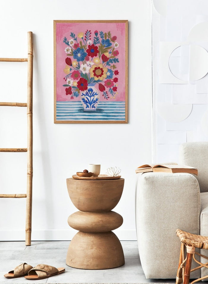 Colorful floral arrangement in a blue and white vase on a pink and blue striped background. Colorful Folk Art Bouquet by Caroline Bonne Müller is a fine art print and wall poster featuring a bright floral arrangement in a patterned vase.