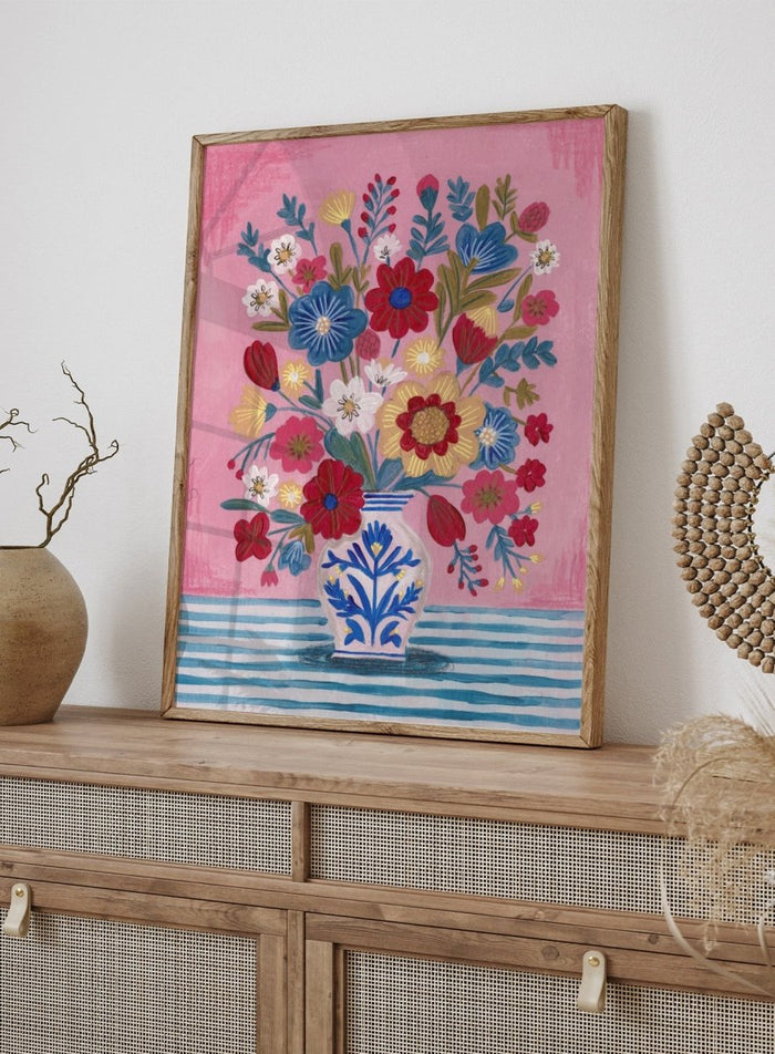 Colorful floral arrangement in a blue and white vase on a pink and blue striped background. Colorful Folk Art Bouquet by Caroline Bonne Müller is a fine art print and wall poster featuring a bright floral arrangement in a patterned vase.