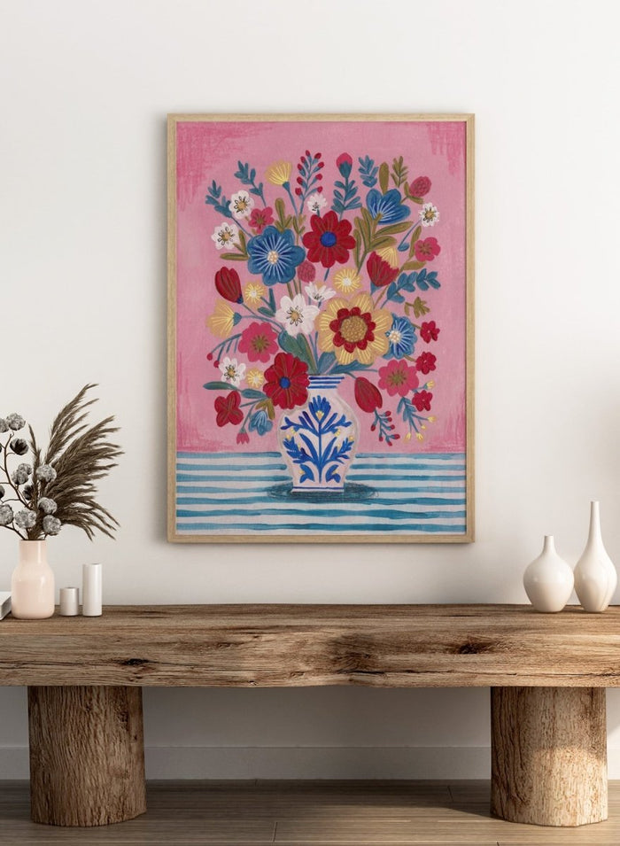 Colorful floral arrangement in a blue and white vase on a pink and blue striped background. Colorful Folk Art Bouquet by Caroline Bonne Müller is a fine art print and wall poster featuring a bright floral arrangement in a patterned vase.