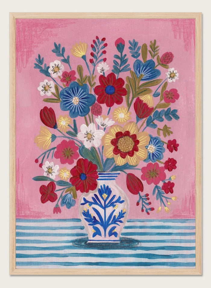 Colorful floral arrangement in a blue and white vase on a pink and blue striped background. Colorful Folk Art Bouquet by Caroline Bonne Müller is a fine art print and wall poster featuring a bright floral arrangement in a patterned vase.
