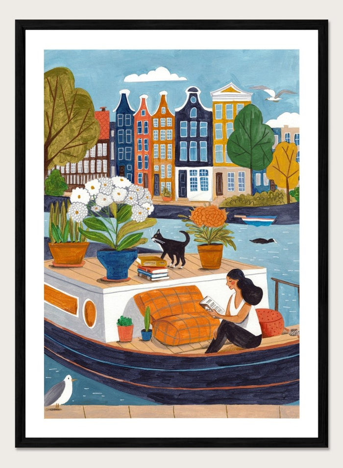 Illustration of a woman on a boat with flowers and a cat, surrounded by colorful houses. Cozy Canal Reading by Caroline Bonne Müller is a fine art print and wall poster featuring a woman reading on a canal boat with colorful European buildings in the background.