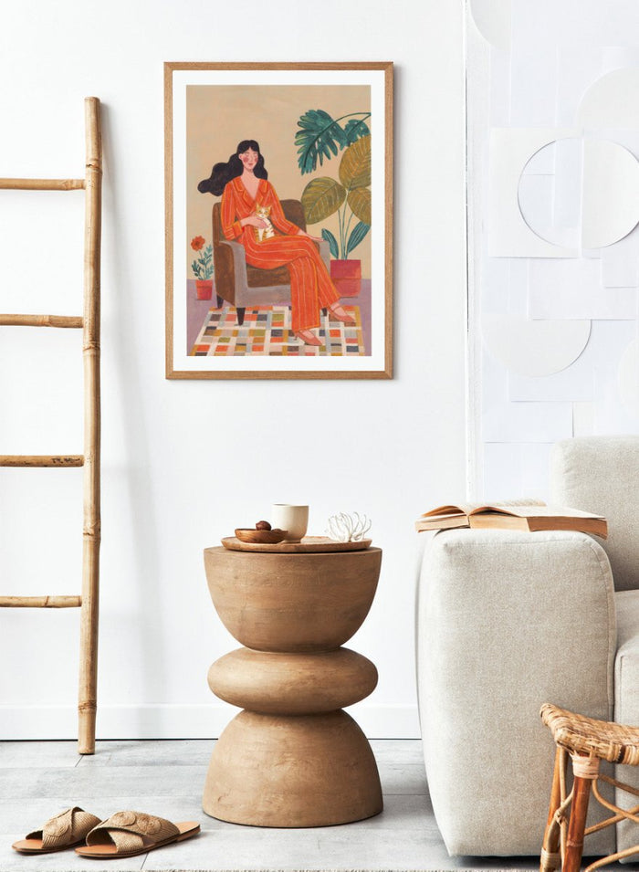 Illustration of a woman in an orange outfit sitting in a chair with plants around her. Cozy Home with Cat by Caroline Bonne Müller is a fine art print and wall poster featuring a woman in an orange outfit sitting with a cat in a warm, plant-filled interior.
