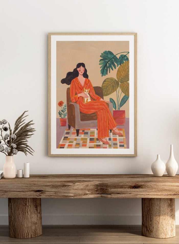 Illustration of a woman in an orange outfit sitting in a chair with plants around her. Cozy Home with Cat by Caroline Bonne Müller is a fine art print and wall poster featuring a woman in an orange outfit sitting with a cat in a warm, plant-filled interior.