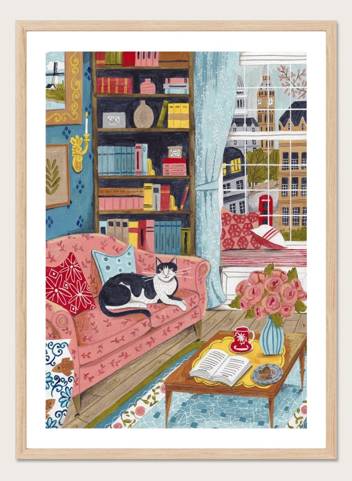 Illustration of a cozy living room with a cat on a pink sofa, bookshelf, and coffee table. Cozy London Cat by Caroline Bonne Müller is a fine art print and wall poster featuring a cat lounging in a colorful living room with a London city view.