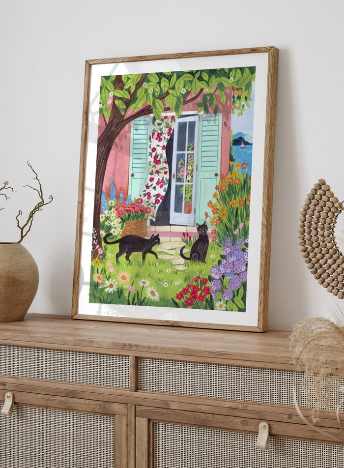 Garden Cats by the Sea by Caroline Bonne Müller is a colorful coastal garden art print featuring cats, florals, and seaside home in a modern aesthetic illustration style.