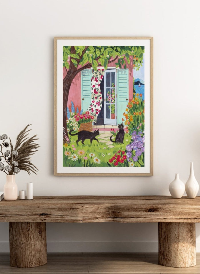 Garden Cats by the Sea by Caroline Bonne Müller is a colorful coastal garden art print featuring cats, florals, and seaside home in a modern aesthetic illustration style.
