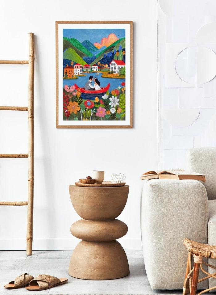 Couple in a red boat on a lake with mountains and houses in the background, surrounded by colorful flowers. Just Married Couple in a Boat by Caroline Bonne Müller is a romantic art print featuring couple illustration, lake scene, colorful flowers, and modern aesthetic wedding artwork.