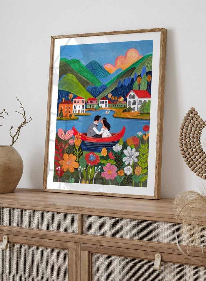 Couple in a red boat on a lake with mountains and houses in the background, surrounded by colorful flowers. Just Married Couple in a Boat by Caroline Bonne Müller is a romantic art print featuring couple illustration, lake scene, colorful flowers, and modern aesthetic wedding artwork.