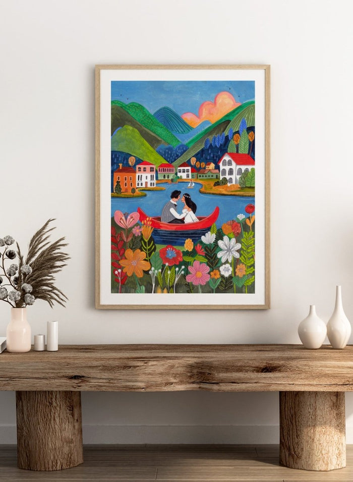 Couple in a red boat on a lake with mountains and houses in the background, surrounded by colorful flowers. Just Married Couple in a Boat by Caroline Bonne Müller is a romantic art print featuring couple illustration, lake scene, colorful flowers, and modern aesthetic wedding artwork.
