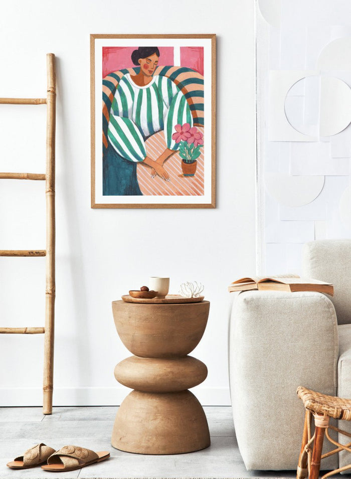 Artistic illustration of a person holding a potted plant with a colorful background. Peaceful Woman Home by Caroline Bonne Müller is a fine art print and wall poster of a woman seated indoors with flowers and striped patterns.