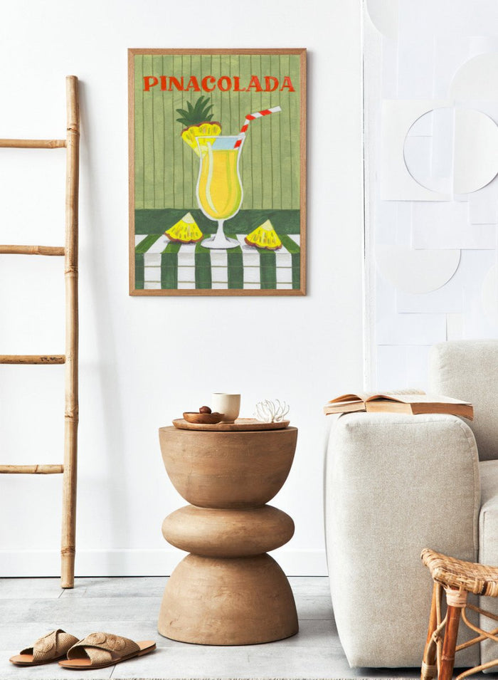 Illustration of a pina colada drink with pineapple slices on a checkered tablecloth. Piña Colada Summer Drink by Caroline Bonne Müller is a fine art print and wall poster of a pineapple cocktail with striped straw and green table setting.