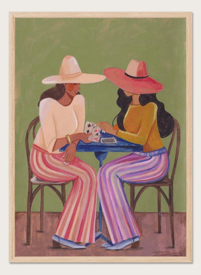Two women playing cards at a table with colorful clothing and hats against a green background. Stylish Women Play Cards by Caroline Bonne Müller is a fine art print and wall poster featuring two fashionable women playing cards at a table.