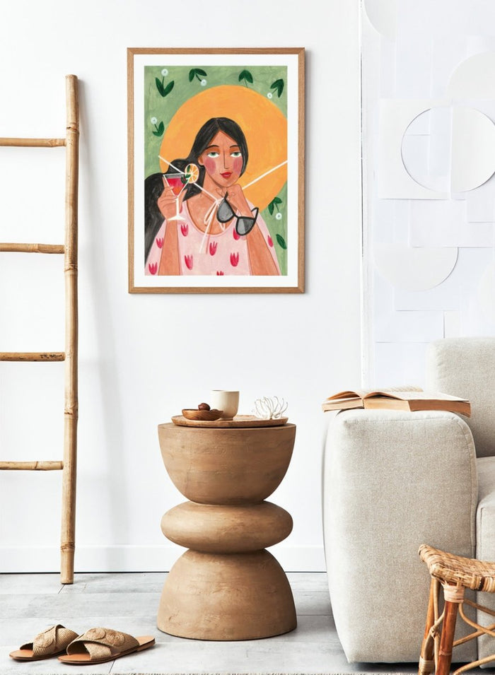 Illustration of a woman holding a cocktail and sunglasses with a sun and foliage background. Summer Woman Cocktail Hat by Caroline Bonne Müller is a fine art print and wall poster featuring a woman holding a cocktail with a bold yellow hat and bright summer colors.