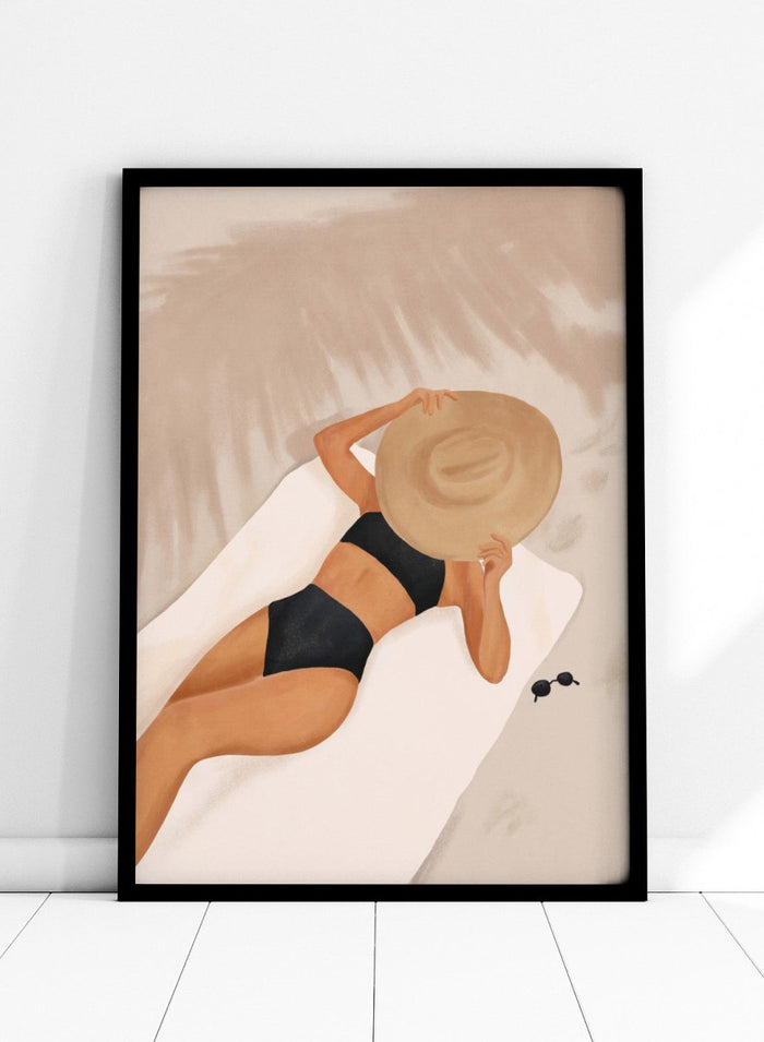 Woman in black bikini and straw hat lying on a towel with sunglasses nearby. Beach Day Relaxation by City Art is a modern beach art print featuring a woman in a black swimsuit, oversized sun hat, soft sand, and warm neutral tones.