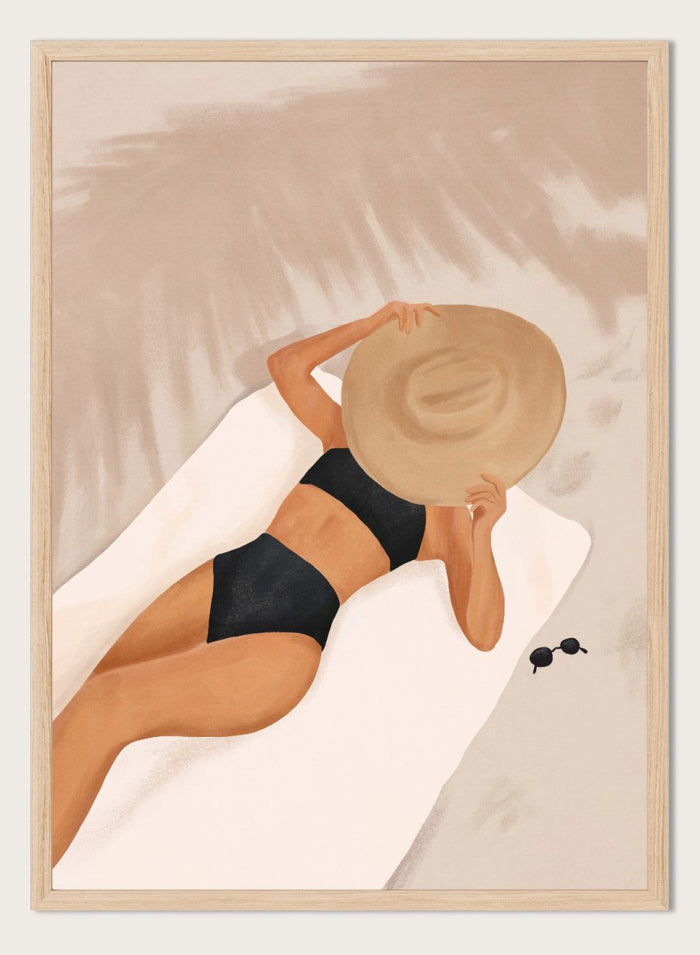 Woman in black bikini and straw hat lying on a towel with sunglasses nearby. Beach Day Relaxation by City Art is a modern beach art print featuring a woman in a black swimsuit, oversized sun hat, soft sand, and warm neutral tones.