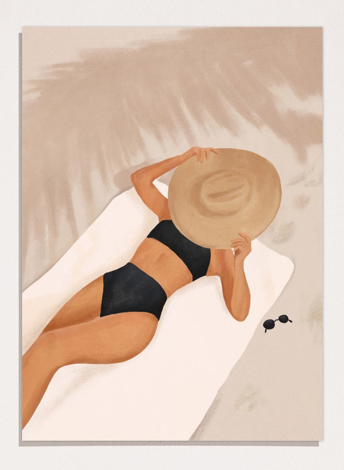 Woman in black bikini and straw hat lying on a towel with sunglasses nearby. Beach Day Relaxation by City Art is a modern beach art print featuring a woman in a black swimsuit, oversized sun hat, soft sand, and warm neutral tones.