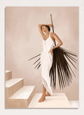 Woman in a white dress standing on a staircase with a palm leaf design. Elegant Tropical Serenity by City Art features a woman in a flowing white dress and palm leaves, bringing organic living, tropical style, and warm neutral tones into the home.