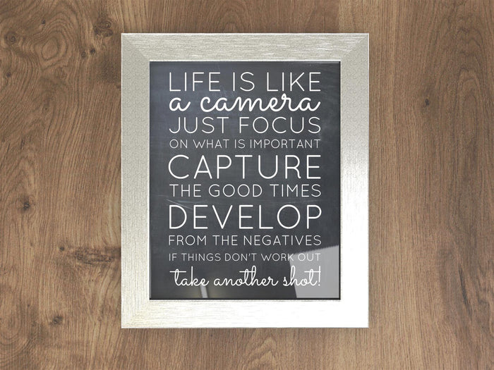Chrome picture frame displaying an inspirational quote about life and photography on a wooden background.