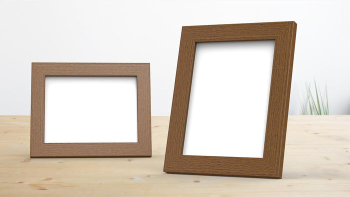 Two dark brown picture frames displayed on a wooden table, one larger and one smaller, with blank white spaces.