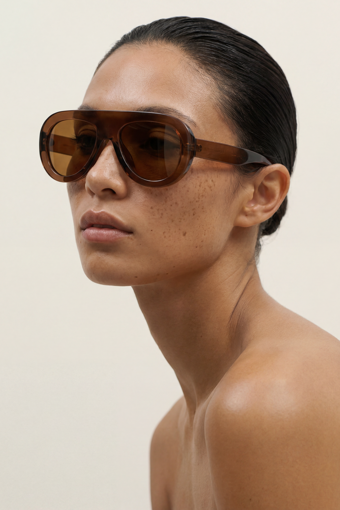 Woman wearing brown AVIATOR sunglasses against a plain background