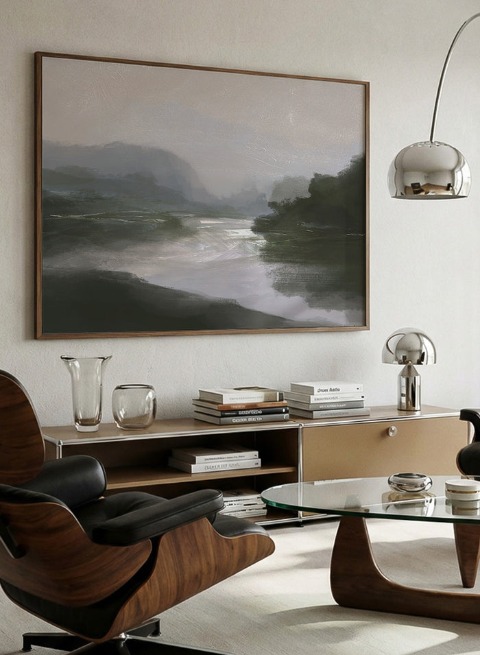 A framed landscape art print depicting a misty river scene with dark green hills, a reflective river, and a pale gray sky. Shop Tranquillitas by Dan Hobday, a contemporary landscape wall art print featuring reflective water, distant hills, dark green trees, and soft gray tones.