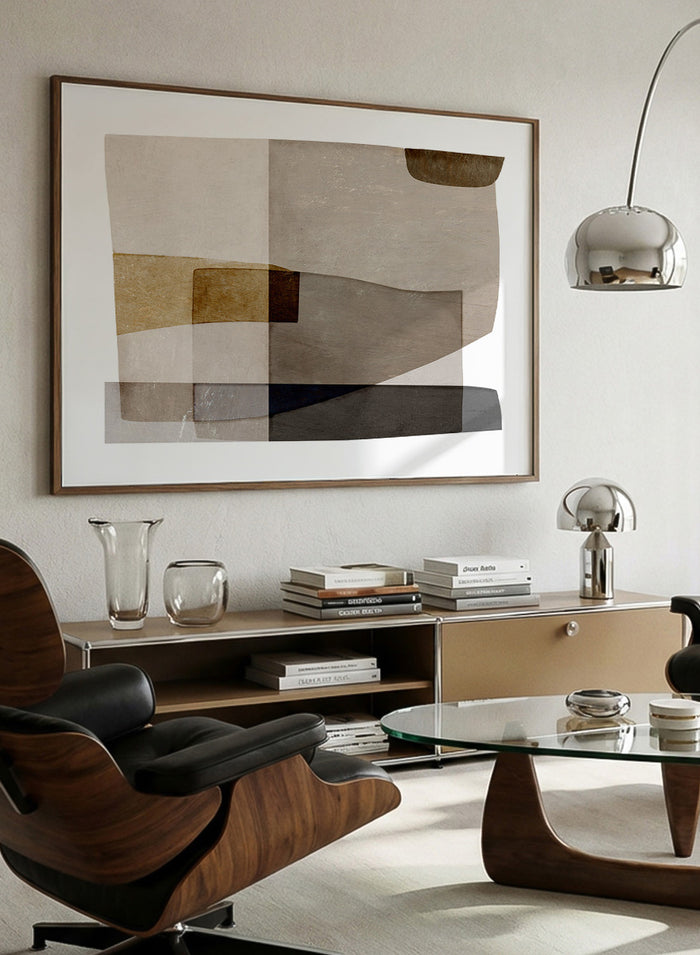 Framed abstract wall art featuring layered geometric shapes in beige, taupe, brown, gray, and black on a white mat, shown against a light warm gray background. Shop Transform by Dan Hobday, a contemporary abstract wall art print featuring layered geometric forms, soft brown and taupe tones, and textured neutral detail.