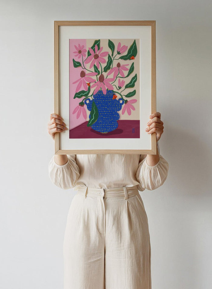 Artistic depiction of a blue vase with pink flowers on a pink background. Cone Flowers in a Pot by Dirkie Nell is a colorful floral art print with pink blooms, butterflies, and a bold blue vase. Officially licensed wall poster.