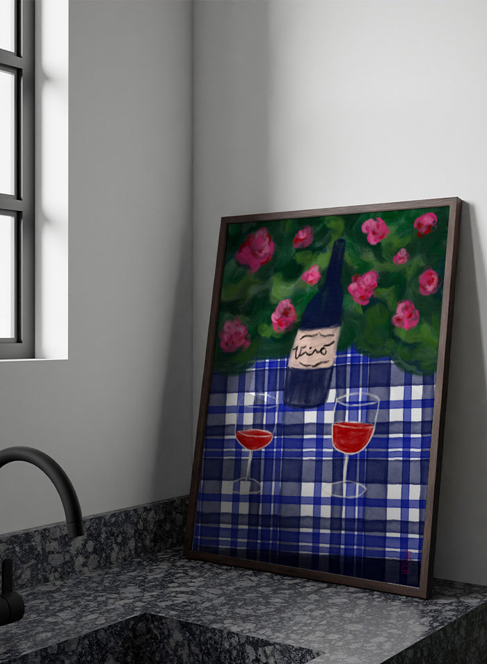 A painted still life scene featuring a dark wine bottle labeled 'vino' on a blue-and-white plaid tablecloth, with two glasses of red wine and pink flowers against a green background. Shop Garden Wine Picnic by Dirkie Nell, a colorful still life art print featuring red wine, blue gingham, pink roses, and a warm summer garden mood.