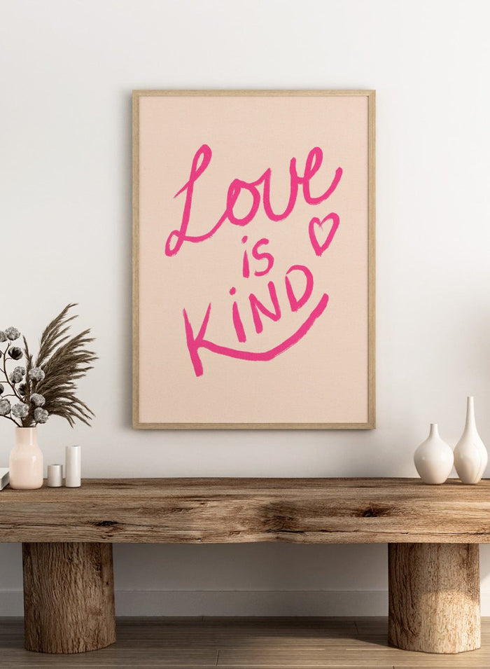 Pink text 'Love is Kind' with a heart on a light pink background. Love Is Kind by Dirkie Nell is a pink typography art print with handwritten lettering and heart detail. A joyful modern love wall poster.