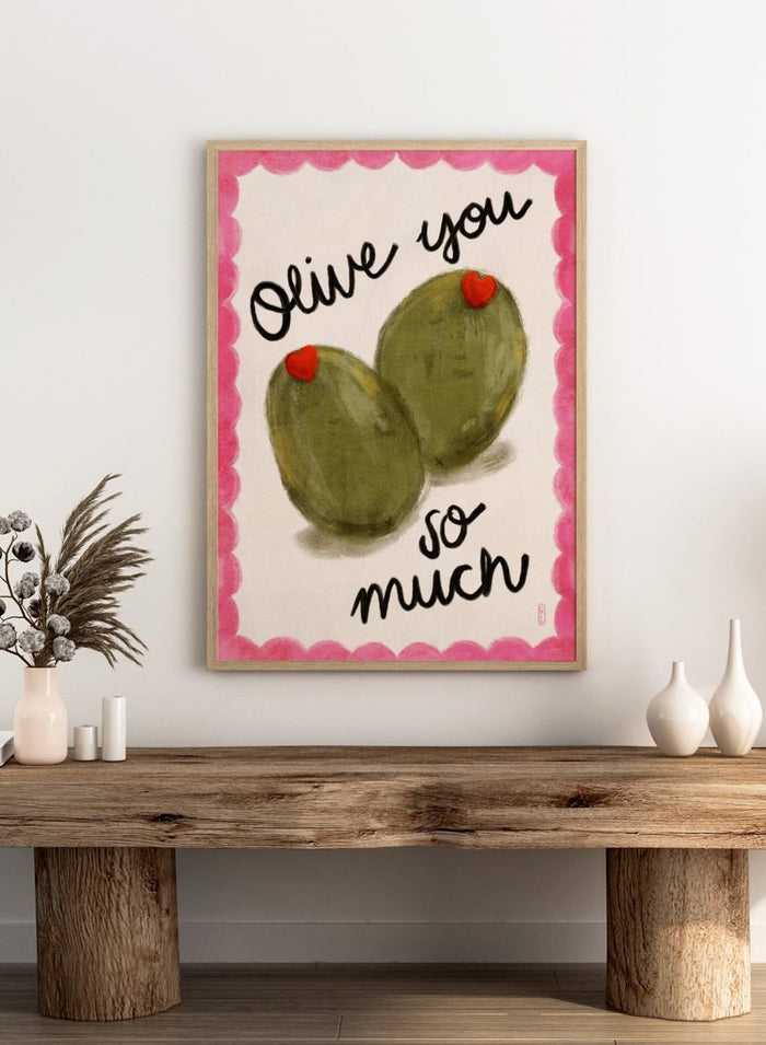 Two olives with red hearts and text 'Olive you so much' on a pink and white background. Olive You So Much by Dirkie Nell is a playful food art print featuring hand painted olives, pink accents, handwritten typography, and whimsical kitchen art details.