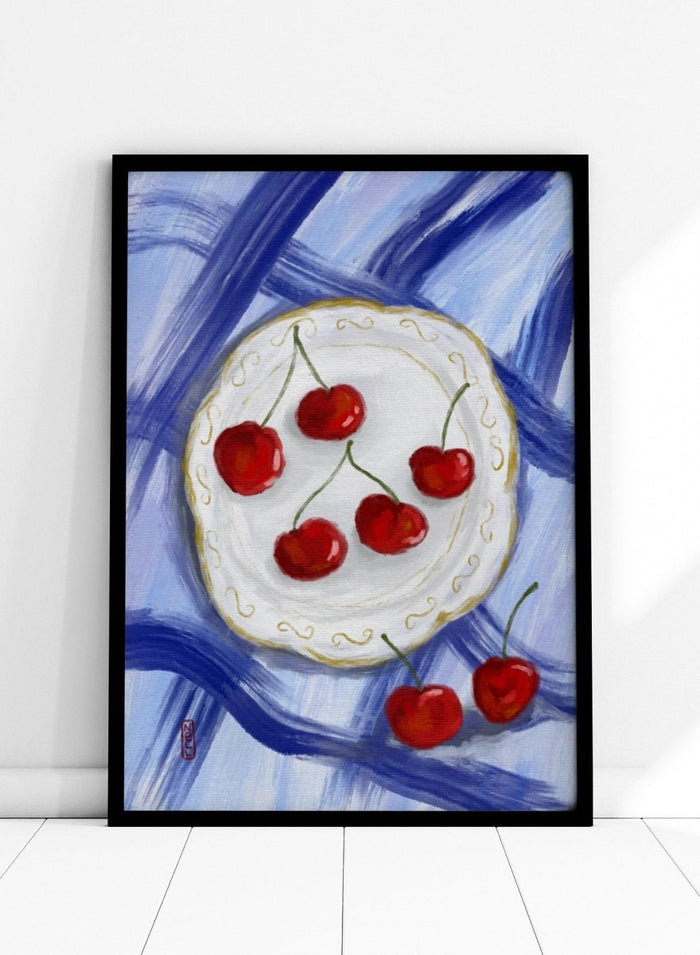 Painting of cherries on a white plate with a blue background. Red Cherries Blue Table by Dirkie Nell is a contemporary fruit still life art print featuring hand painted cherries, blue table linens, and colorful kitchen wall art style.