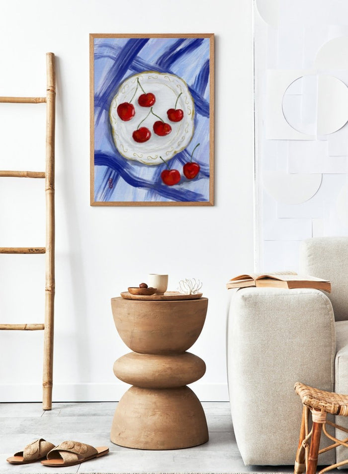 Painting of cherries on a white plate with a blue background. Red Cherries Blue Table by Dirkie Nell is a contemporary fruit still life art print featuring hand painted cherries, blue table linens, and colorful kitchen wall art style.