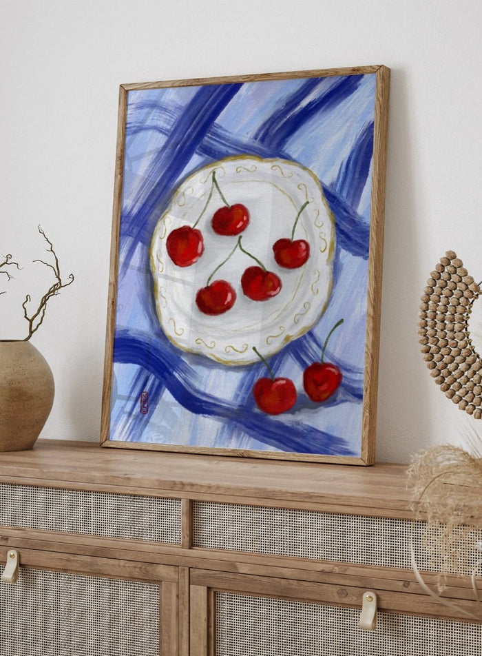 Painting of cherries on a white plate with a blue background. Red Cherries Blue Table by Dirkie Nell is a contemporary fruit still life art print featuring hand painted cherries, blue table linens, and colorful kitchen wall art style.