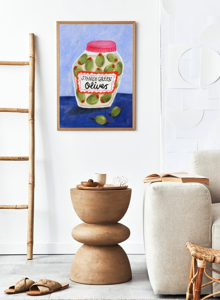 Illustration of a jar of Spanish green olives on a blue background. Spanish Green Olives Jar by Dirkie Nell is a playful food art print featuring hand painted olives, colorful kitchen details, and Mediterranean inspired design.