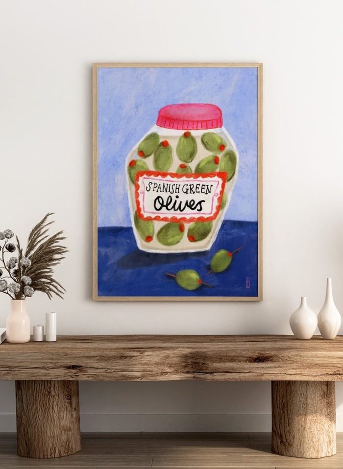Illustration of a jar of Spanish green olives on a blue background. Spanish Green Olives Jar by Dirkie Nell is a playful food art print featuring hand painted olives, colorful kitchen details, and Mediterranean inspired design.