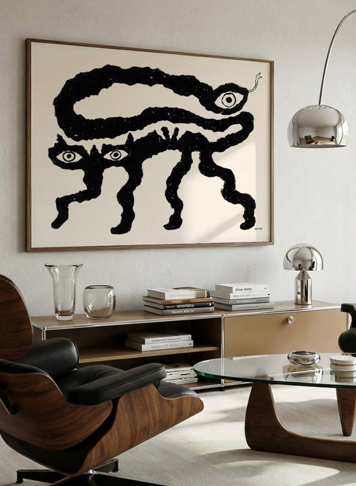 Framed artwork of a black and white creature with cat-like features and snake-like body. I Am Animals by Eden Kalif is a modern minimalist line art print featuring abstract animal forms in a bold black and white contemporary wall poster design.