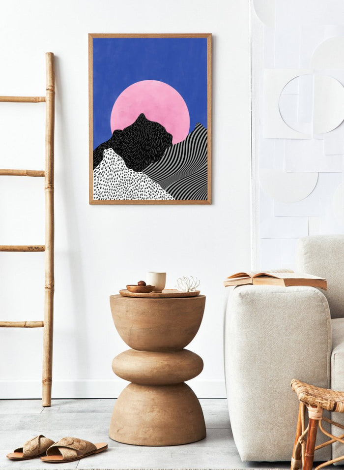 Artistic depiction of mountains with a pink moon in a blue sky. Surreal Peaks View by Elena Ristova is a minimalist abstract landscape print with bold mountains and a pink sun. Officially licensed wall poster with framing.