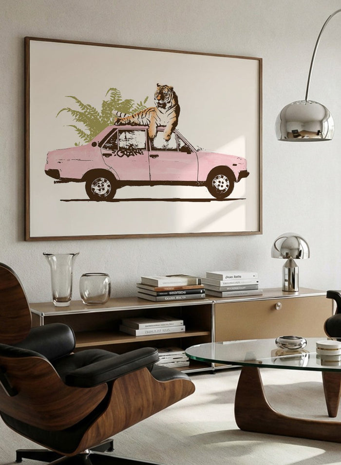 Framed artwork of a tiger in a pink car with greenery on a white background. Tiger On Pink Car by Florent Bodart is a surreal animal art print with a tiger on a vintage car, a modern wall poster with playful, bold, and imaginative design.
