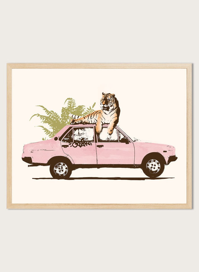 Framed artwork of a tiger in a pink car with greenery on a white background. Tiger On Pink Car by Florent Bodart is a surreal animal art print with a tiger on a vintage car, a modern wall poster with playful, bold, and imaginative design.
