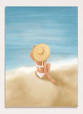 Woman in a white bikini and sun hat sitting on sand looking at ocean. Ocean View Relaxation by Flow Line is a coastal wall art print featuring a woman by the ocean, soft blue tones, beach decor, and relaxed summer style.