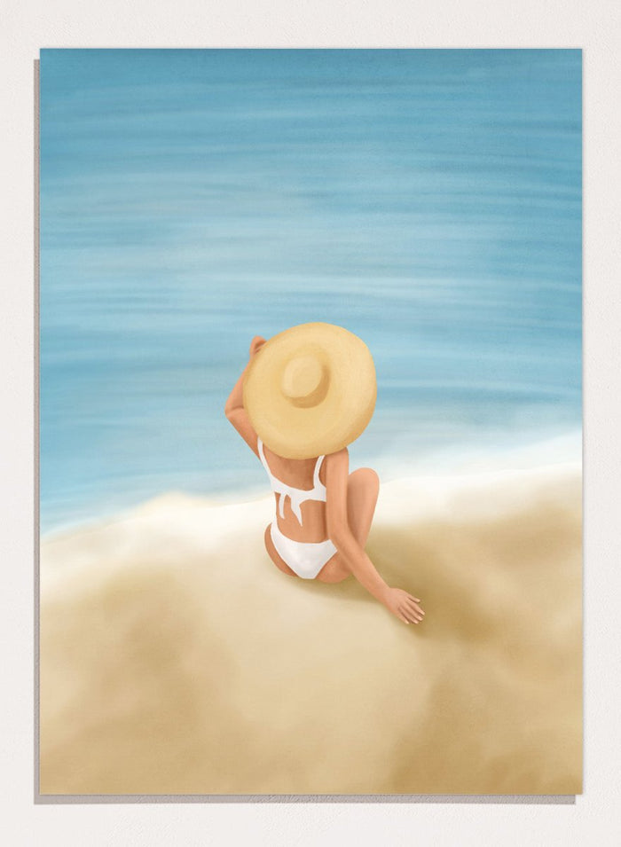 Woman in a white bikini and sun hat sitting on sand looking at ocean. Ocean View Relaxation by Flow Line is a coastal wall art print featuring a woman by the ocean, soft blue tones, beach decor, and relaxed summer style.