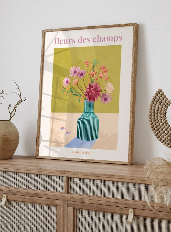 Illustration of a vase with flowers on a green background, featuring the text 'fleurs des champs' and 'couleurs d'ete'. Fleur Des Champs Green by Goed Blauw is a colorful floral art print and wall poster featuring a striped vase with loose flowers on a warm yellow background.