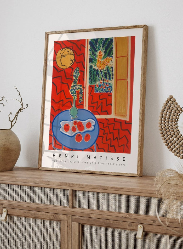 Artistic depiction of a still life scene with a blue table, vase, and fruit, by Henri Matisse. Red Interior, Still Life on a Blue Table by Henri Matisse is a 1947 modern art print featuring bold color, expressive interiors, floral still life details, and iconic French design.