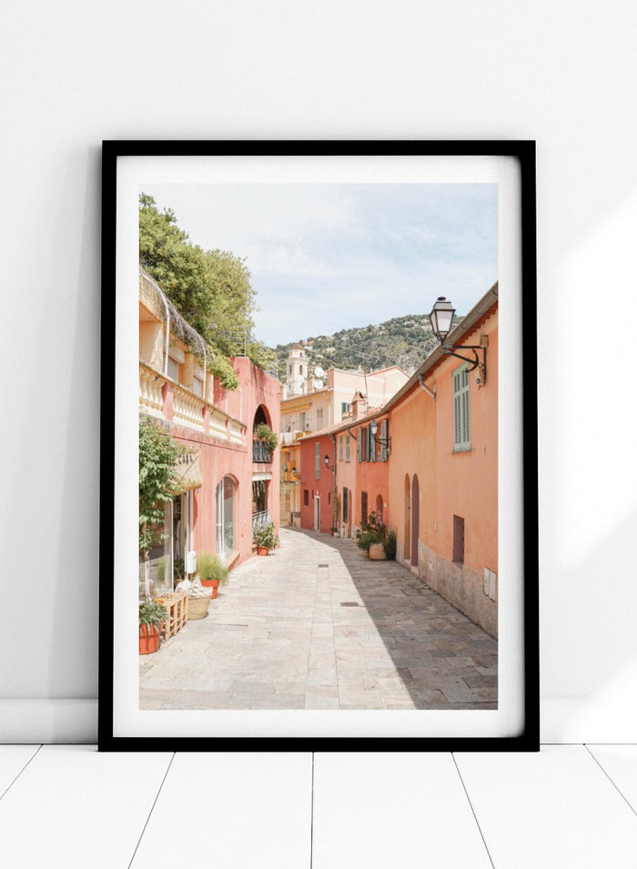 Tiled street with colorful buildings and greenery under a clear blue sky. Colorful Old Town Street by Henrike Schenk is a European travel photography print featuring Mediterranean architecture, pastel buildings, and street wall art.