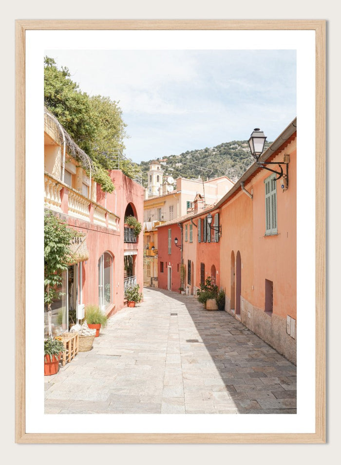 Tiled street with colorful buildings and greenery under a clear blue sky. Colorful Old Town Street by Henrike Schenk is a European travel photography print featuring Mediterranean architecture, pastel buildings, and street wall art.