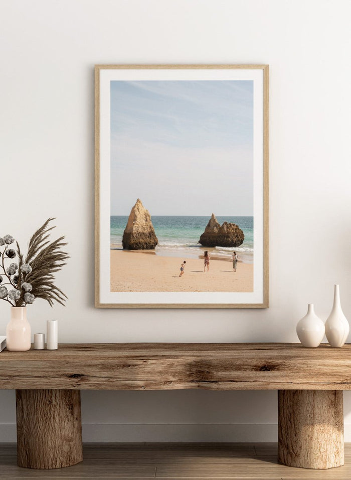 Three people on a beach with large rock formations and clear blue sky. Family Beach Day by Henrike Schenk is a coastal photography print showing a family on a sandy beach with ocean waves and dramatic sea cliffs.