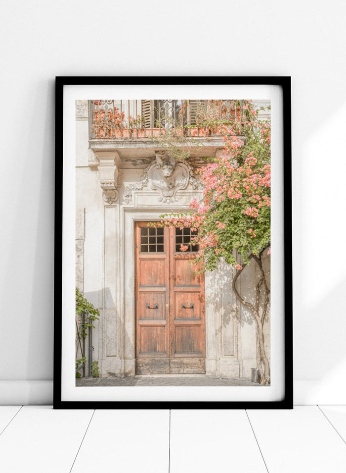 Wooden door with floral decorations on a building facade. Floral Entry by Henrike Schenk is a Mediterranean photography print featuring an old European doorway, blooming flowers, and historic architecture.